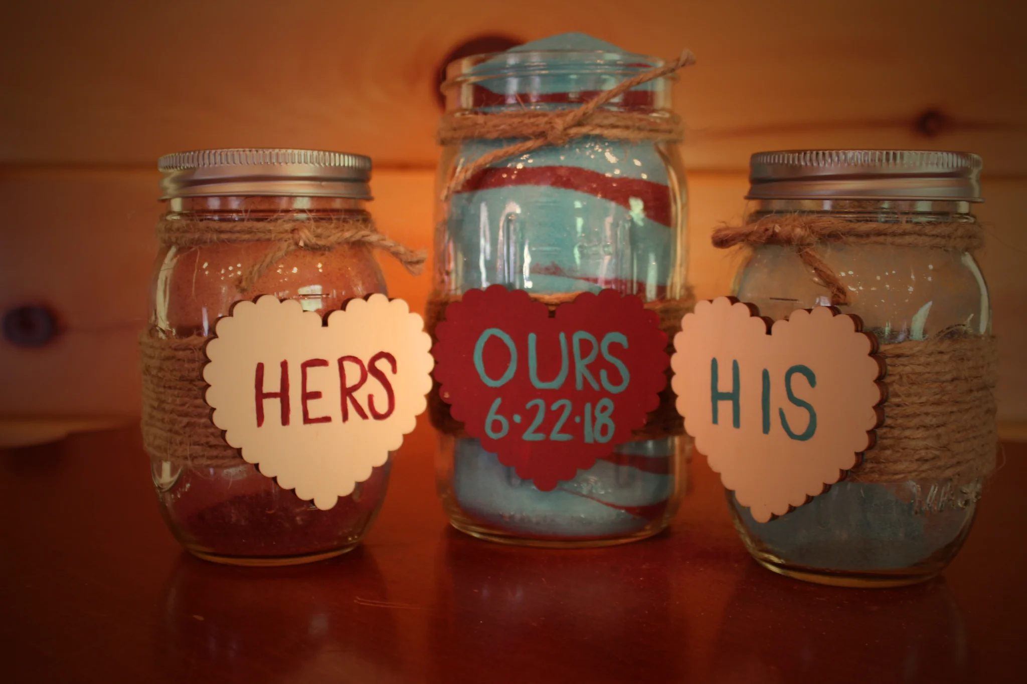 Close up of wedding sand jars labeled 'Hers', 'Ours 6-22-18', and 'His' with twine at Moose Hollow Lodge