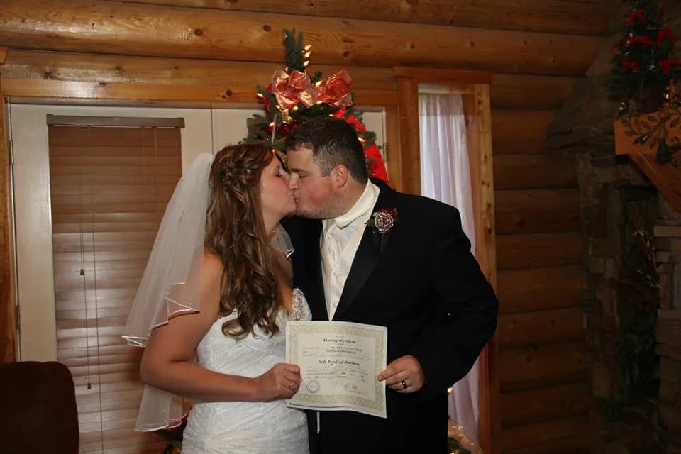 Newlyweds kissing and holding marriage certificate in rustic log cabin venue at Moose Hollow Lodge in Pigeon Forge