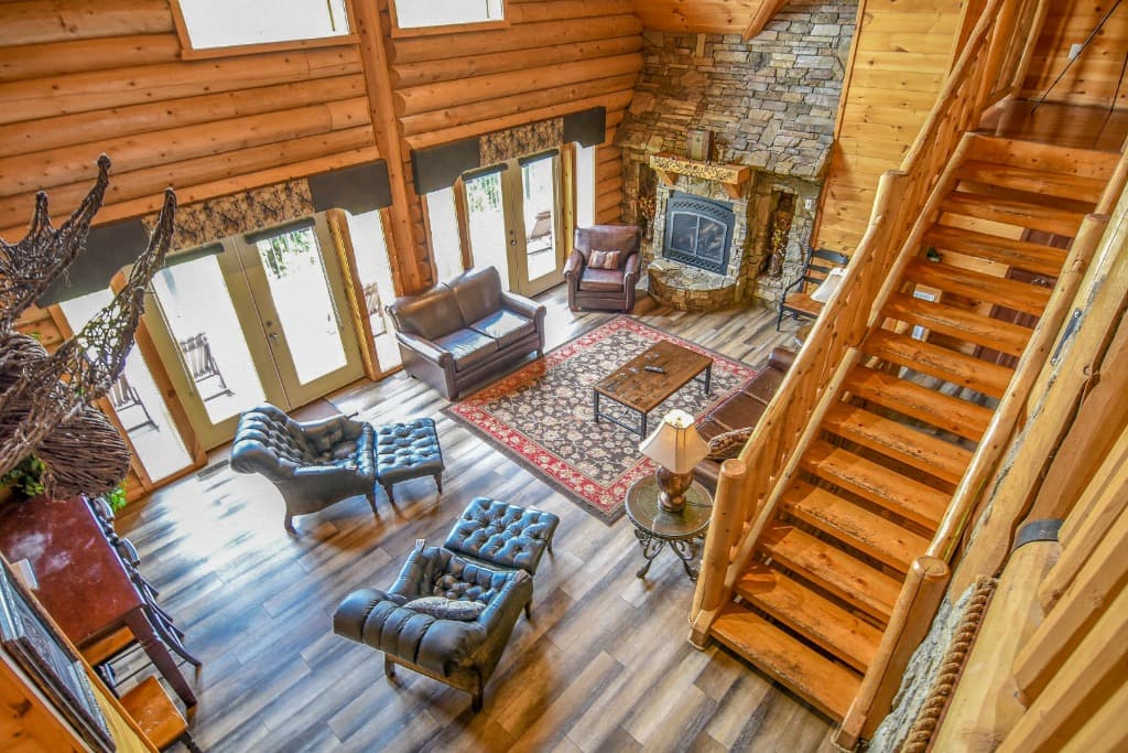 Spacious rustic living room with leather sofas, stone fireplace, and log stairs at Moose Hollow Lodge in Sevierville
