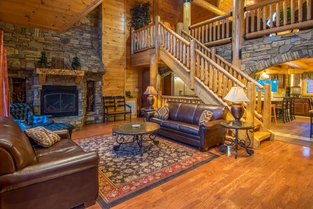 Spacious living room with leather sofas, stone fireplace, and log stairs at Moose Hollow Lodge in Sevierville