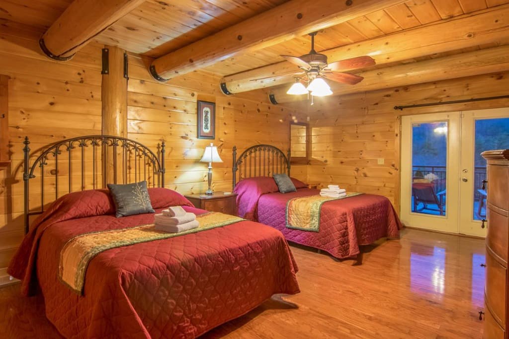Rustic log cabin bedroom with two queen beds and deck access at Moose Hollow Lodge in Sevierville
