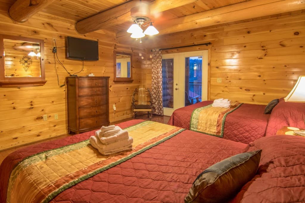 Log cabin bedroom with two beds, wooden dresser, and deck access at Moose Hollow Lodge in Sevierville
