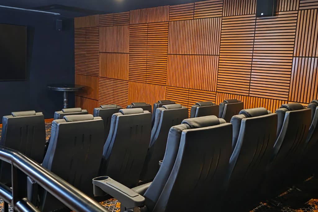 Luxury vacation rental theater room with comfortable black recliner seating, large screen, and acoustic wood slat walls.